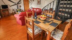 A cozy living room with a wooden dining table, red sofa, and a staircase. - Primose Cottage (Milford Haven)