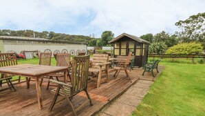 A patio area with wooden furniture, including tables and chairs, and a small shed. - Primose Cottage (Milford Haven)