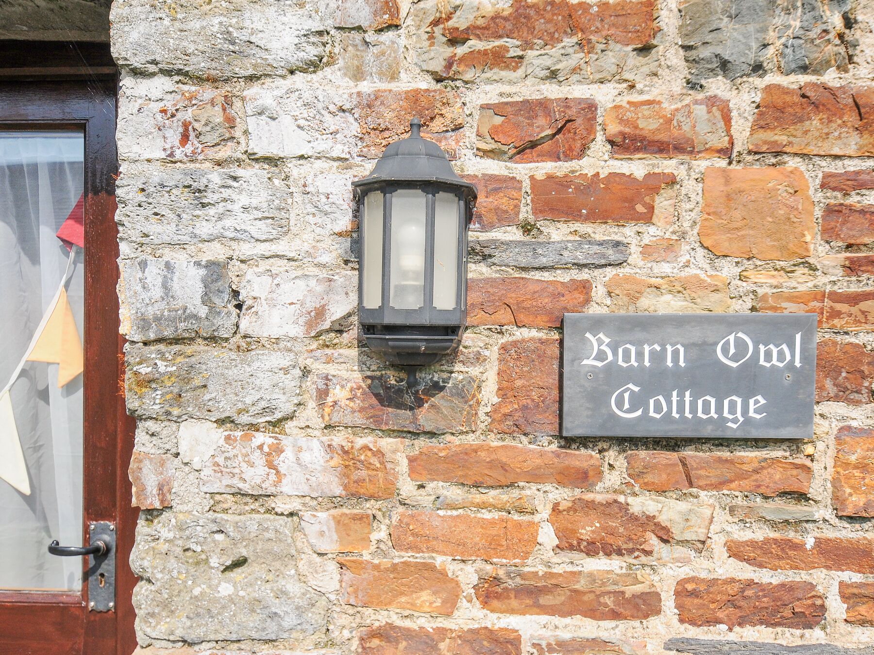 Een stenen muur met een bord waarop staat: 'Barn Owl Cottage'.