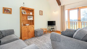 Ein Wohnzimmer mit einem Holzkasten, grauen Sofas, einem Fernseher und einem Balkon mit Vorhängen.