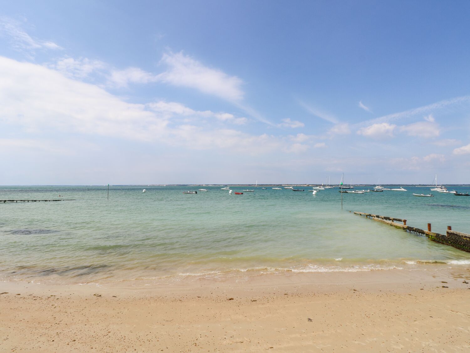 A beach with a clear sky, calm sea, and several boats anchored in the distance.