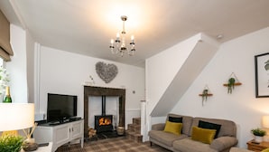A living room with a fireplace, a sofa, a television, and a chandelier. - Pemba Cottage (Skipton)