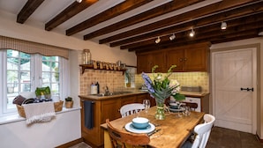 A kitchen with wooden beams, a window with a view, and a dining table set with chairs. - Pemba Cottage (Skipton)