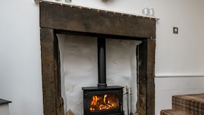 A fireplace with a black stove, a stack of firewood, and a basket of logs. - Pemba Cottage (Skipton)