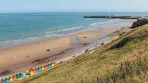 Une plage côtière avec une jetée, des cabanes de plage et un phare.