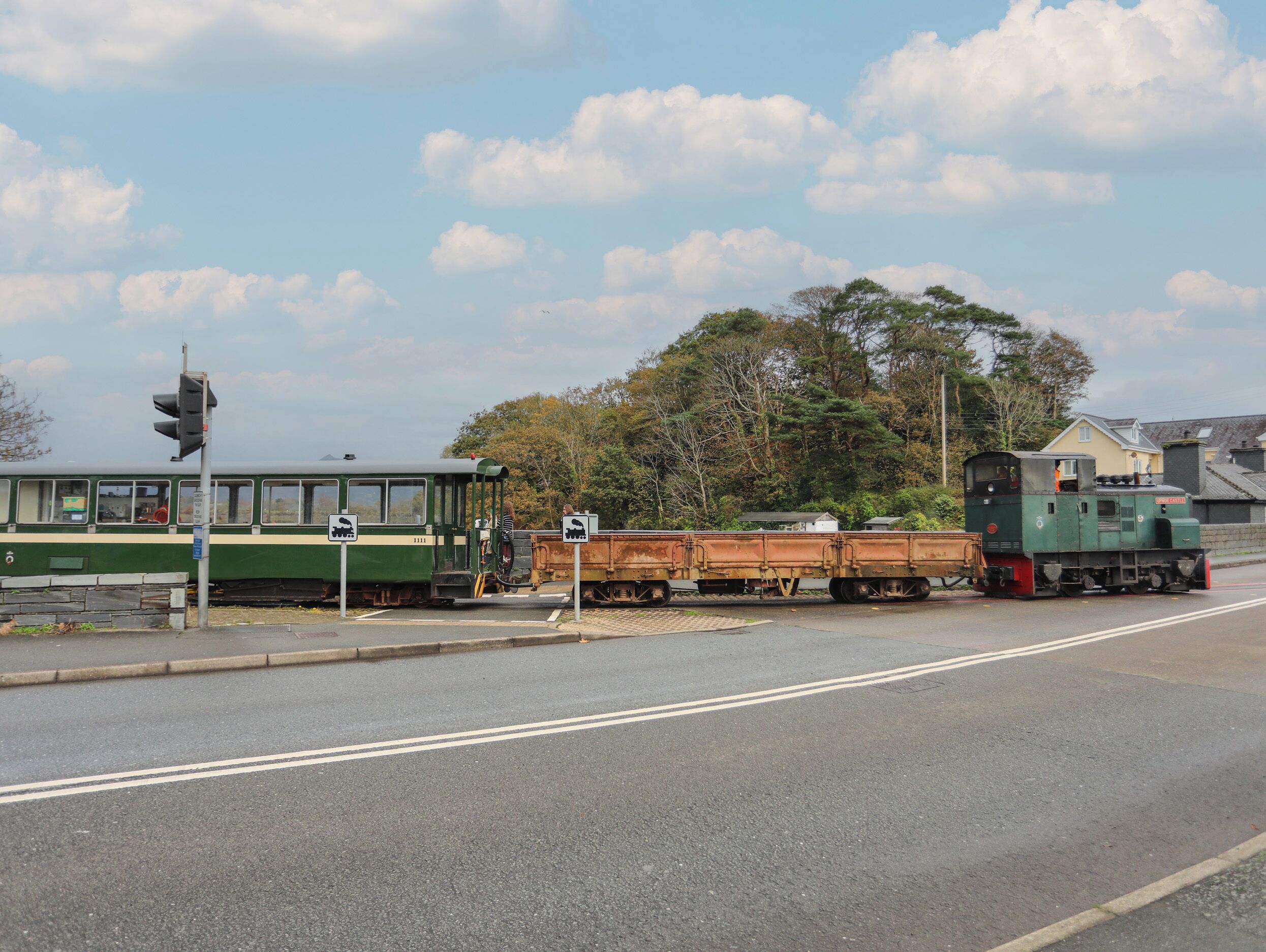 A green train with a flatbed car and a caboose at a railway crossing.