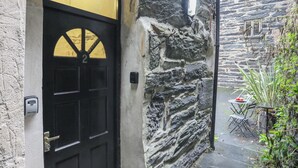 A black door with a yellow window, a stone wall, and a small outdoor seating area with a table and chairs. - The Old Cornhill (Porthmadog)