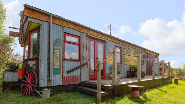 Un edificio antiguo y rústico con fachada de metal corrugado, ventanas de marco rojo y una terraza de madera.
