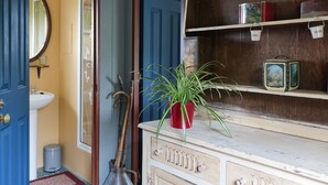 Un baño con una puerta azul, un lavabo blanco, un espejo, una planta roja en maceta y un estante con objetos antiguos.
