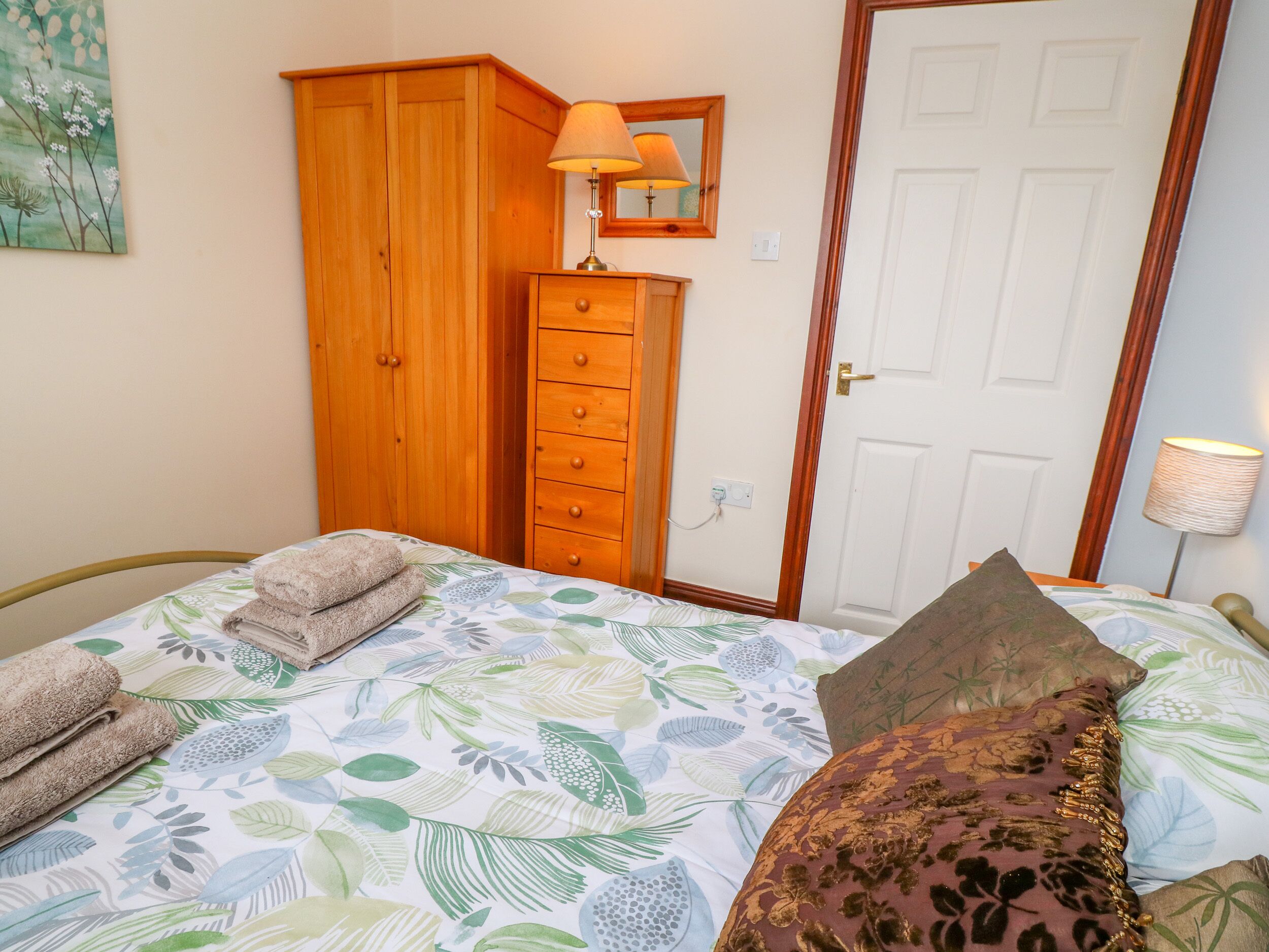 A bedroom with a bed, a wooden wardrobe, a nightstand with a lamp, and a door.