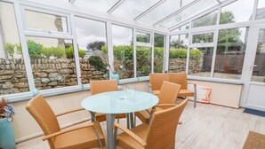 A conservatory with wicker furniture and a glass table, surrounded by stone walls and greenery. - Mossley Cottage (Penzance)