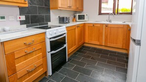 A compact kitchen with wooden cabinets, a built-in oven, a microwave, and a sink. - Mossley Cottage (Penzance)