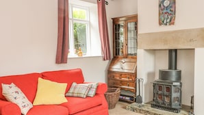 A cozy living room with a red sofa, a wooden cabinet, and a fireplace. - Cutlers Cottage (Matlock)