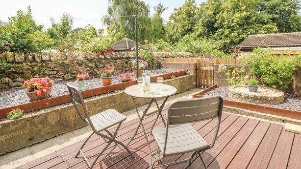 An outdoor patio with a table and two chairs, surrounded by potted plants and a stone wall. - Cutlers Cottage (Matlock)