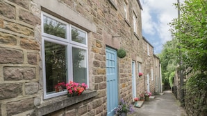 A stone building with multiple windows and doors, a narrow pathway, and potted flowers. - Cutlers Cottage (Matlock)