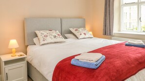 A neatly made bed with floral pillows, a red blanket, and folded towels. - Cutlers Cottage (Matlock)
