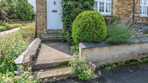 A brick house with a white door, a small garden with flowers, and a neatly trimmed hedge. - Wren Cottage (Oakham)