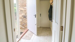 A hallway with a white door, a brick wall, and a hat hanging on the door. - Wren Cottage (Oakham)