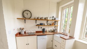 A kitchen with white cabinets, a dishwasher, wooden countertops, and a window with a view of greenery. - Wren Cottage (Oakham)