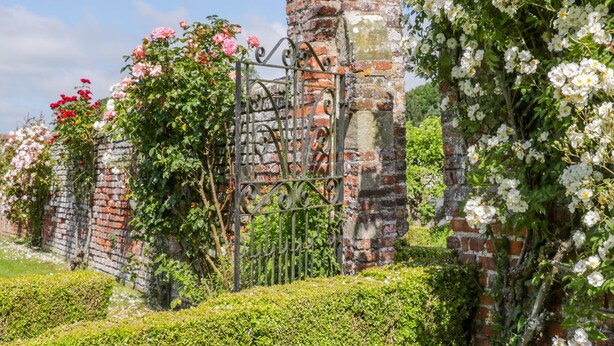 A garden with a wrought iron gate, brick pillars, and flowering plants. - Bella's Cottage (Driffield)