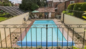 A rectangular swimming pool with a metal fence, surrounded by a brick building and greenery. - Bella's Cottage (Driffield)