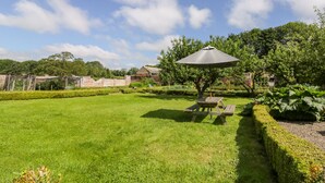 A well-maintained garden with a picnic table and umbrella, surrounded by neatly trimmed hedges and trees. - Bella's Cottage (Driffield)