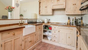A kitchen with wooden cabinets, a sink, and a window above the countertop. - Drumhead Bothy (Banchory)