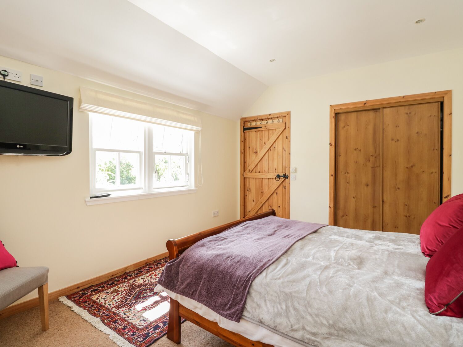 A bedroom with a bed, a TV mounted on the wall, a window, and a door.