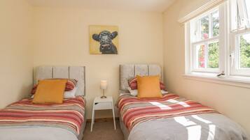 Een slaapkamer met twee bedden, een klein nachtkastje met een lamp, een schilderij aan de muur, en een raam met uitzicht op groen.