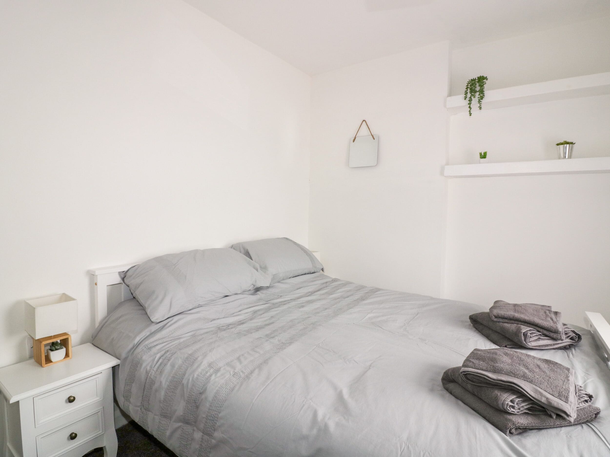 A minimalist bedroom with a bed, a nightstand, a small plant, and a mirror on the wall.