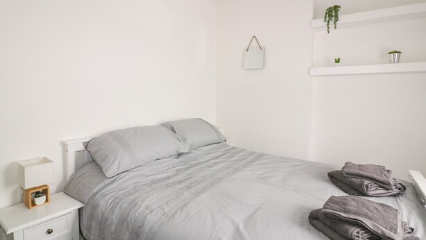 Ein schlicht eingerichtetes Schlafzimmer mit Bett, Nachttisch, einer kleinen Pflanze und einem Spiegel an der Wand.