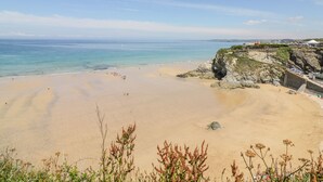 Ein weiter Sandstrand mit klarem, blauem Wasser, felsigen Klippen und spärlicher Vegetation.