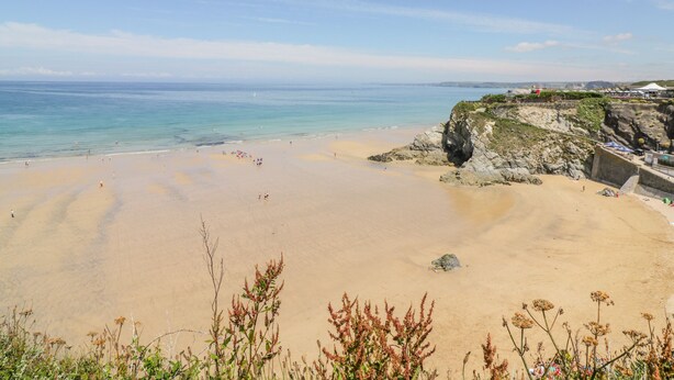 A wide sandy beach with clear blue water, rocky cliffs, and sparse vegetation. - Fistral Quay (Newquay)