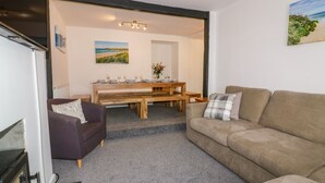 A living room with a sofa, a dining table with chairs, and a fireplace. - Fistral Quay (Newquay)