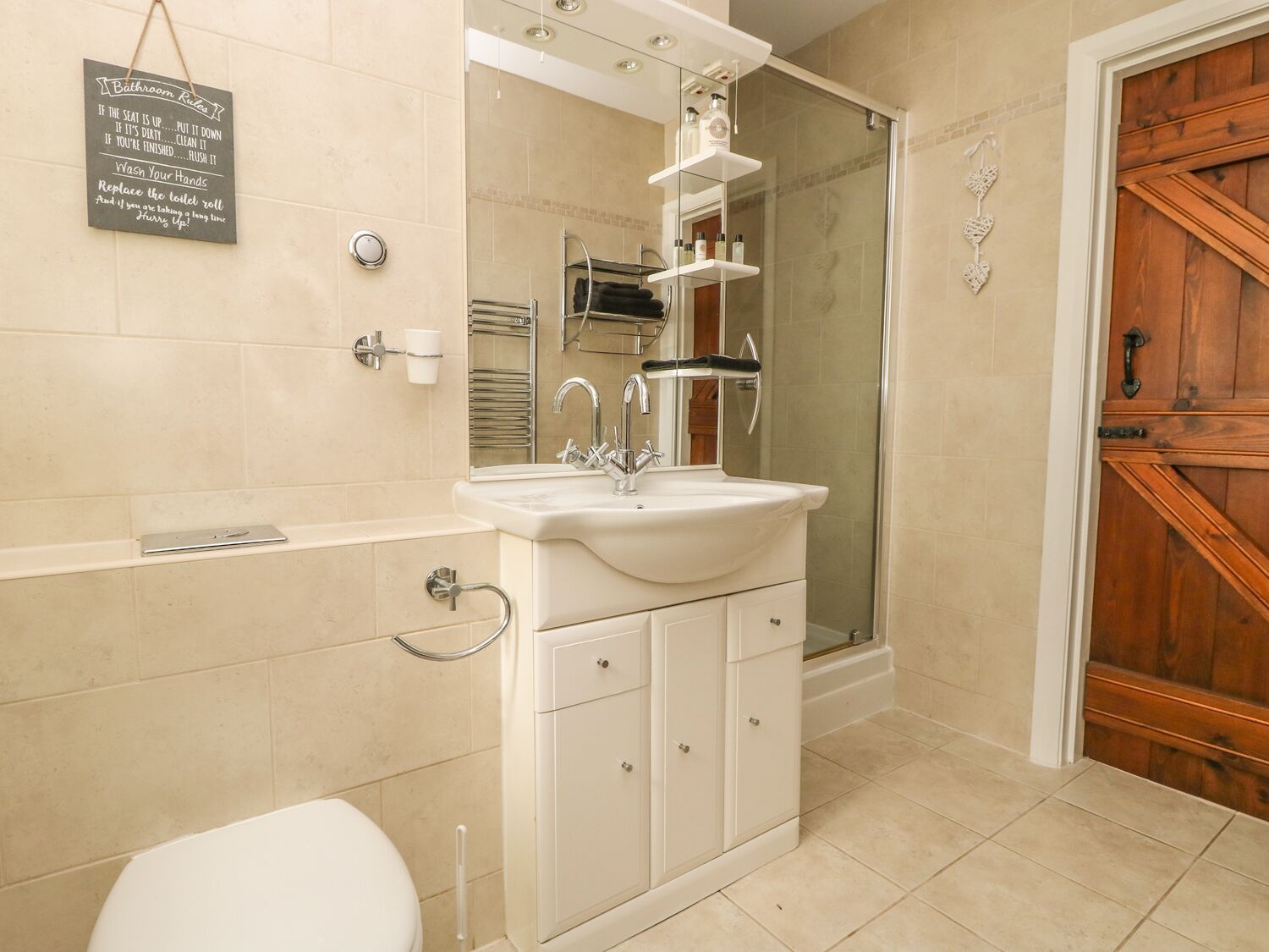 A bathroom with a sink, mirror, and toilet. There is a sign on the wall with bathroom etiquette.
