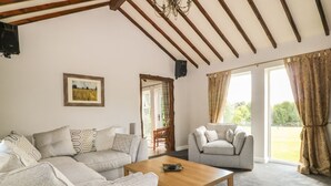 A spacious living room with a large sofa, a smaller armchair, a wooden coffee table, and a painting on the wall. - The Barn at Orchard Farm (York)