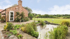 A brick house with a garden, a pond, and a fenced field. - The Barn at Orchard Farm (York)