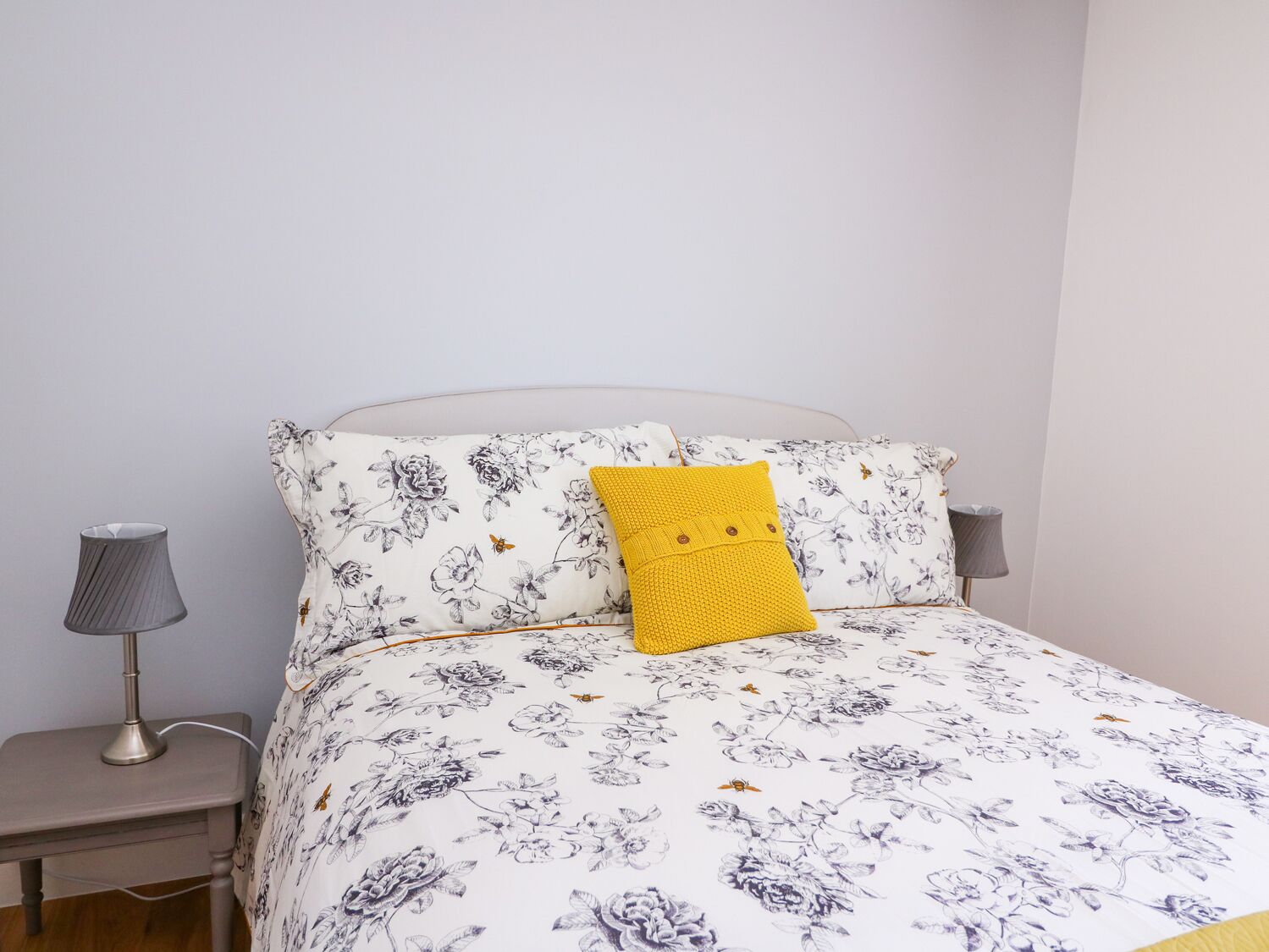 A neatly made bed with floral bedding, a single yellow pillow, and two bedside lamps.