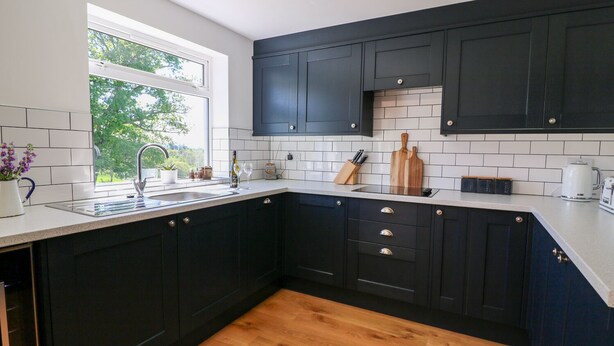 A modern kitchen with dark cabinets, a white countertop, and a wooden floor. - Owl Cottage (Llandrindod Wells)