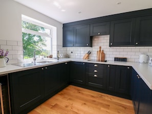 Una cocina moderna con armarios oscuros, encimera blanca y suelo de madera.