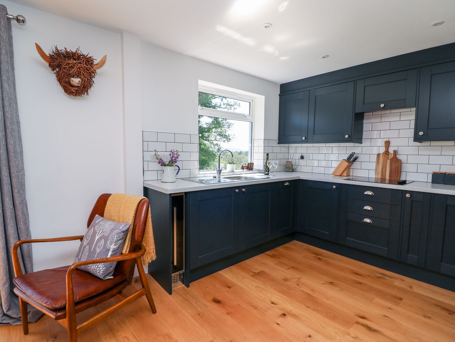 Une cuisine moderne avec des meubles bleu foncé, un plan de travail blanc et un plancher en bois.