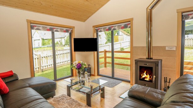A living room with a fireplace, leather sofas, a glass coffee table, and large sliding glass doors leading to a backyard. - Chale Farm Lodge (Ventnor)