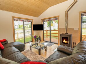 A living room with a fireplace, leather sofas, a glass coffee table, and large sliding glass doors leading to a backyard. - Chale Farm Lodge (Ventnor)