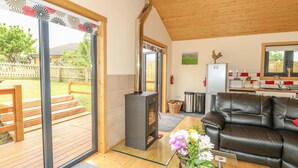 A cozy living room with a fireplace, a black leather sofa, a dining area with a kitchen in the background, and a sliding glass door leading to a deck. - Chale Farm Lodge (Ventnor)