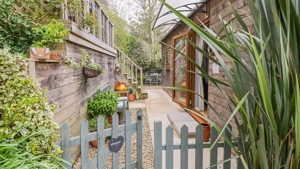 Een houten huis met een tuin, een houten hek en een bord met een welkomstboodschap.