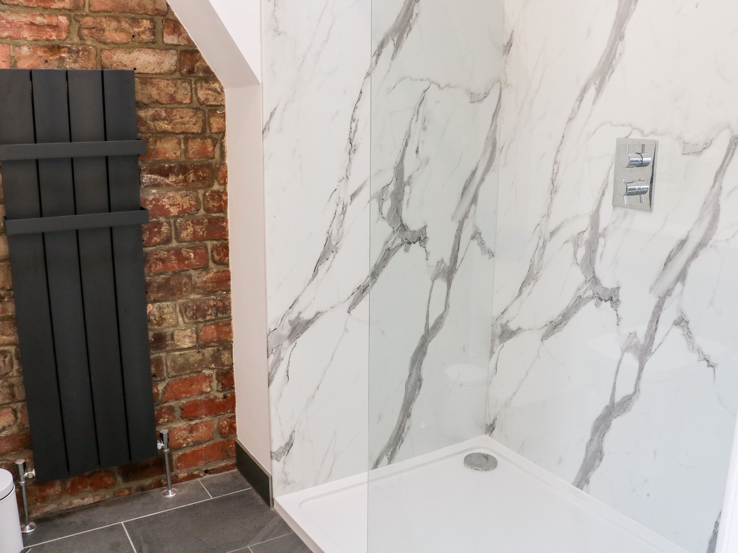 A bathroom with a marble wall, a black radiator, and a white sink.