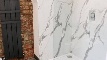 Un baño con pared de mármol, radiador negro y lavabo blanco.