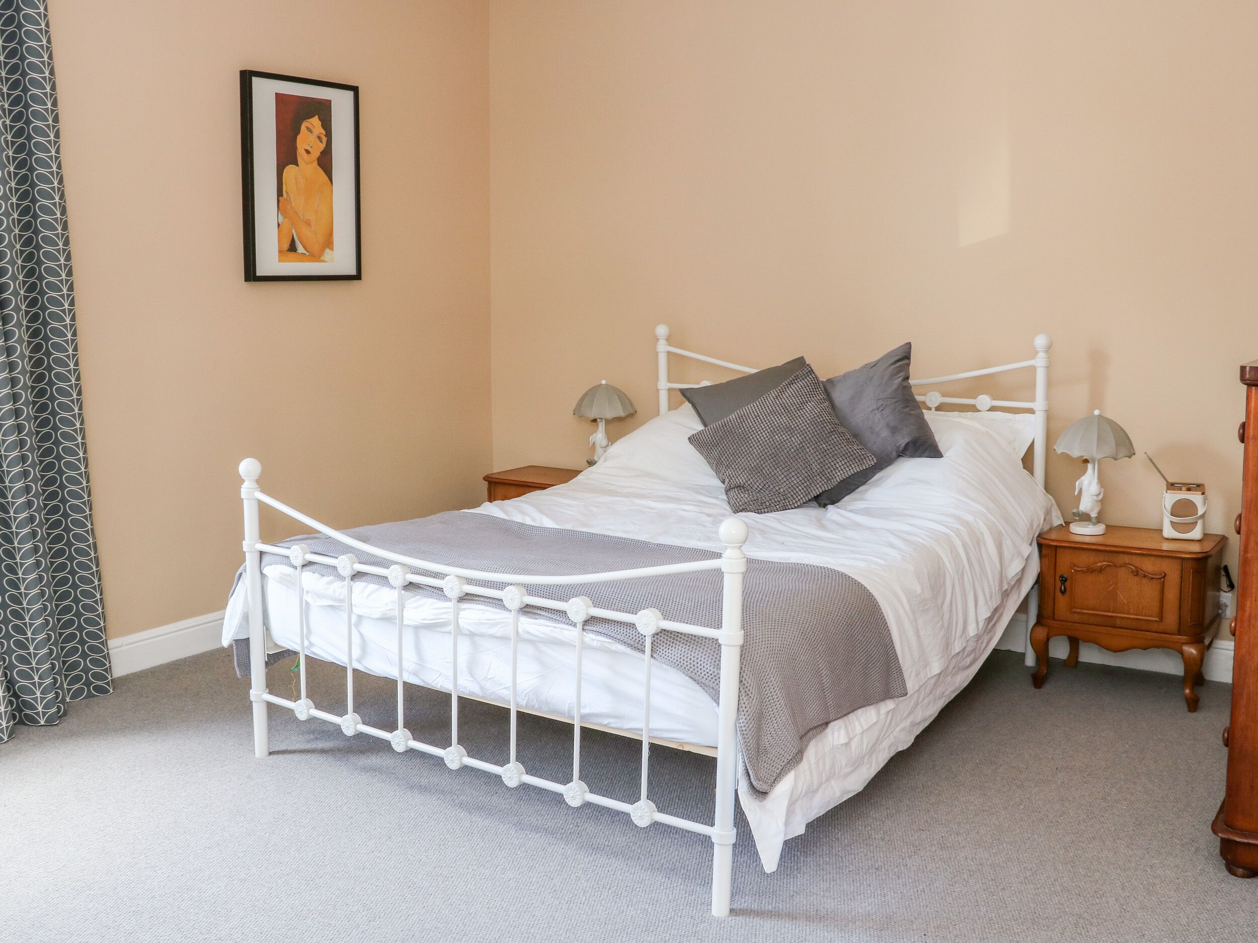 A neatly made bed with a white metal frame, two bedside tables with lamps, and a framed picture on the wall.