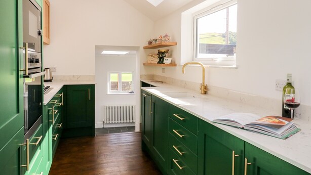 A kitchen with green cabinets, a white countertop, a window, and a bottle of wine on the counter.