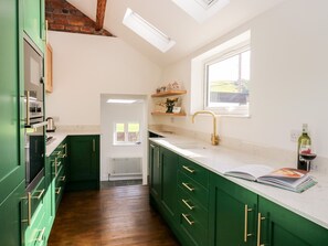 A kitchen with green cabinets, a white countertop, a window, and a bottle of wine on the counter. - West View Cottage (Settle)